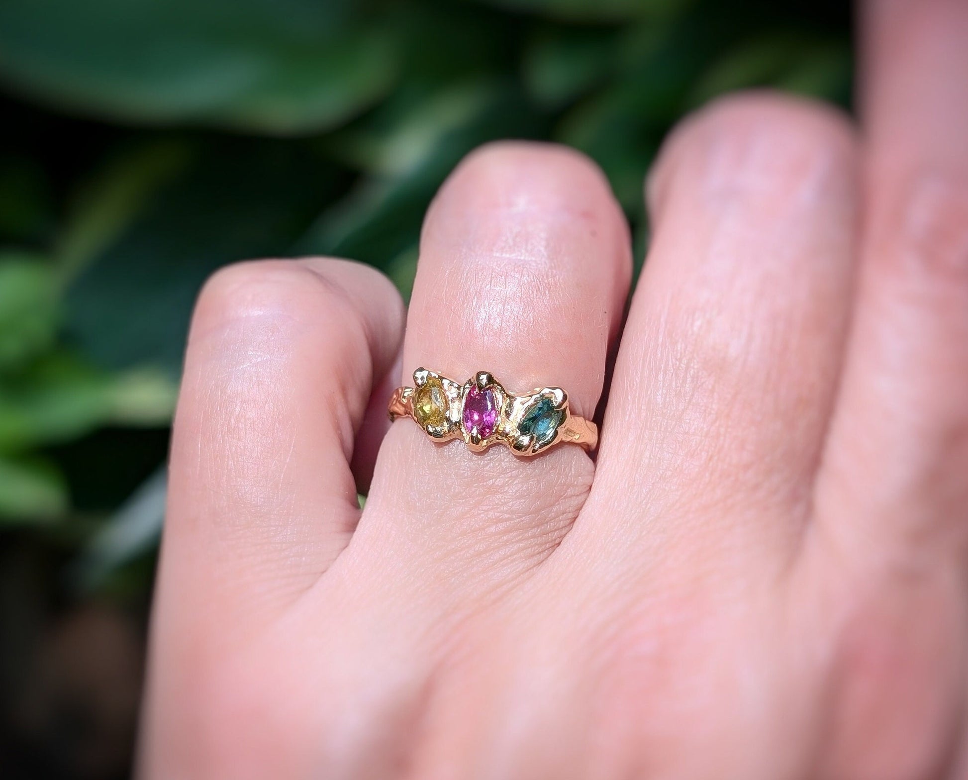Solid gold multi Tourmaline ring featuring three colorful gemstones on a hand against a natural background.