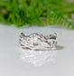 Handcrafted sterling silver molten textured wedding band on a reflective surface with greenery in the background.