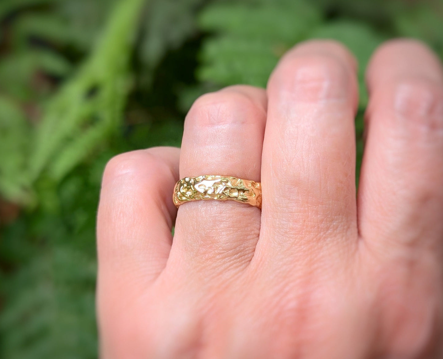 Handcrafted molten gold textured wedding ring placed on a finger, highlighting its rustic elegance and organic form.