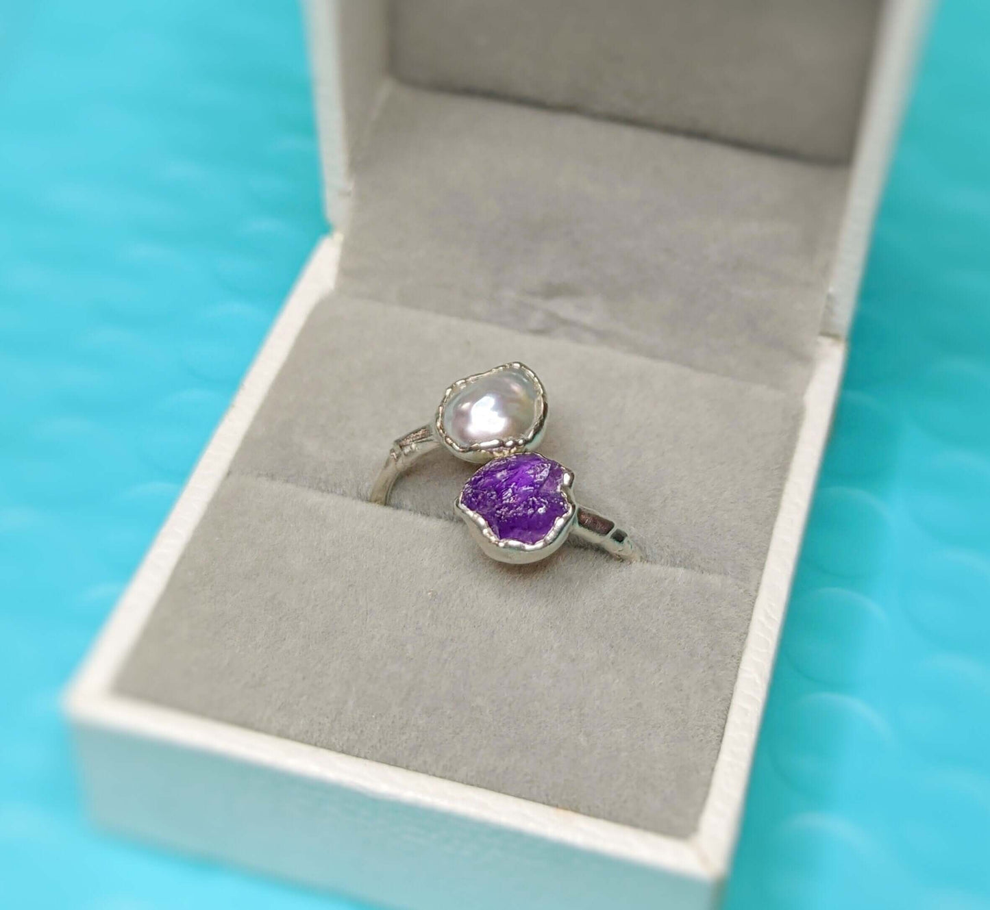 Toi et Moi raw gemstone ring featuring purple and white stones, displayed in a jewelry box.