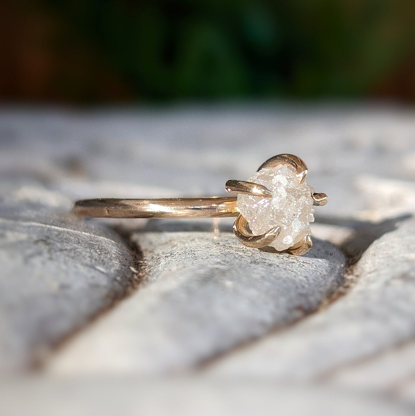 Raw diamond engagement ring in gold setting, showcasing unique uncut diamond design on natural background.