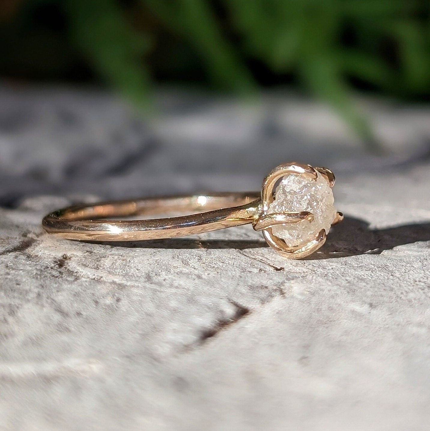 Raw diamond engagement ring in 14k gold setting, showcasing a natural, uncut diamond on a textured surface.