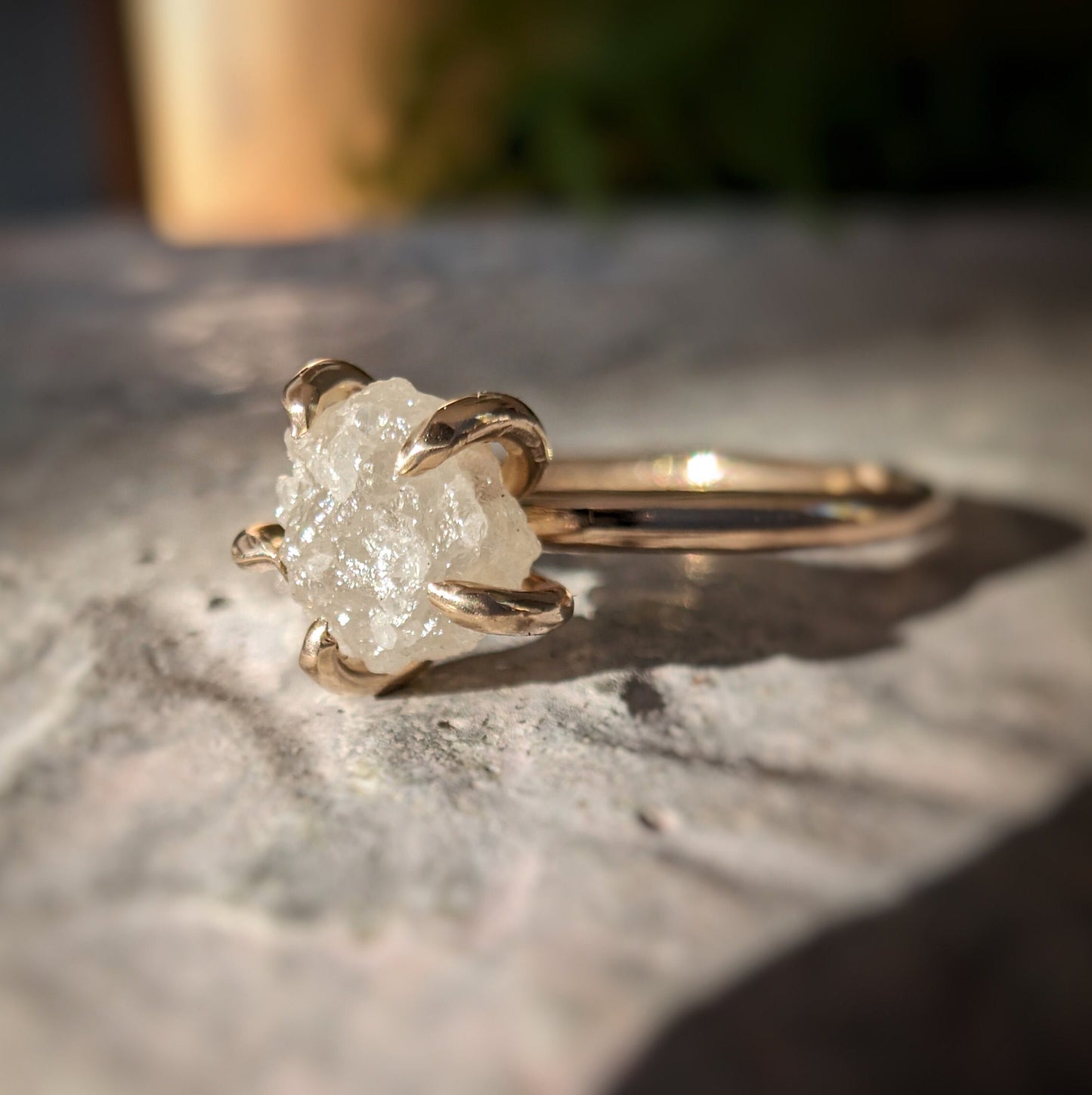 Raw diamond engagement ring in gold, showcasing unique natural beauty on stone background.
