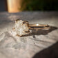 Raw diamond engagement ring in gold, showcasing unique natural beauty on stone background.