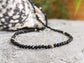 Handcrafted Black Spinel bead necklace with shimmering black beads and gold accents on a textured surface.
