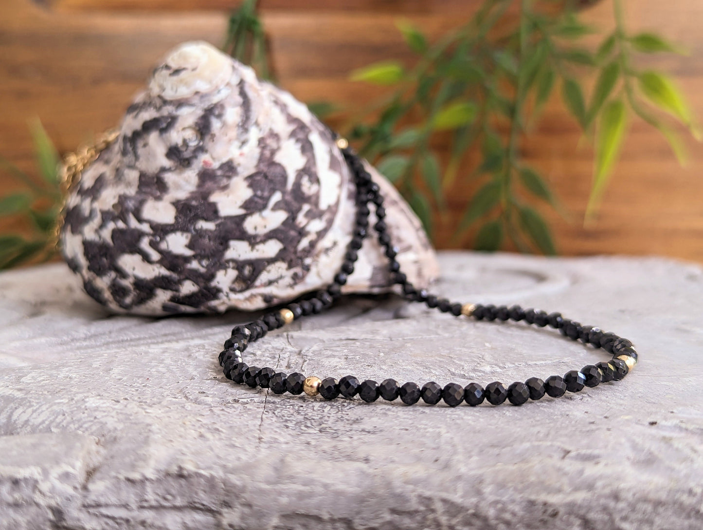 Elegant black Spinel bead necklace on a textured surface with a decorative shell in the background.