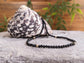 Elegant black Spinel bead necklace on a textured surface with a decorative shell in the background.