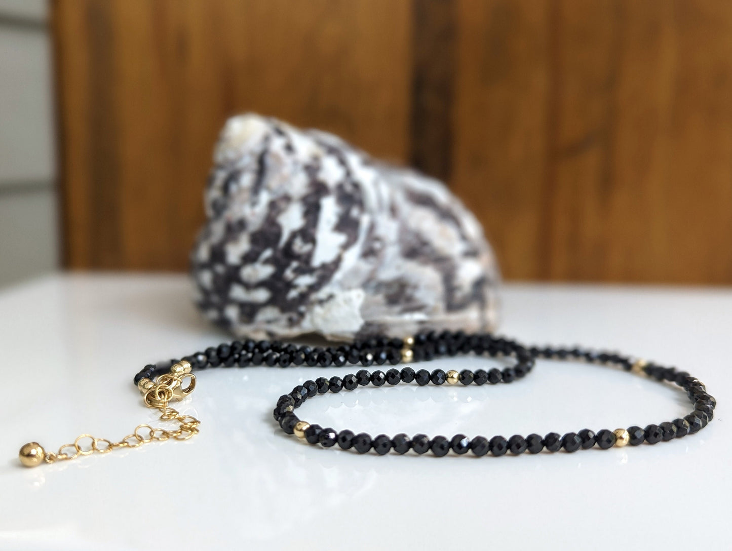 Handcrafted black spinel bead necklace with gold accents displayed next to a seashell.