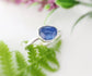 Rustic blue Kyanite silver ring on a green fern background, handcrafted with a unique rose-cut stone and sterling silver band.