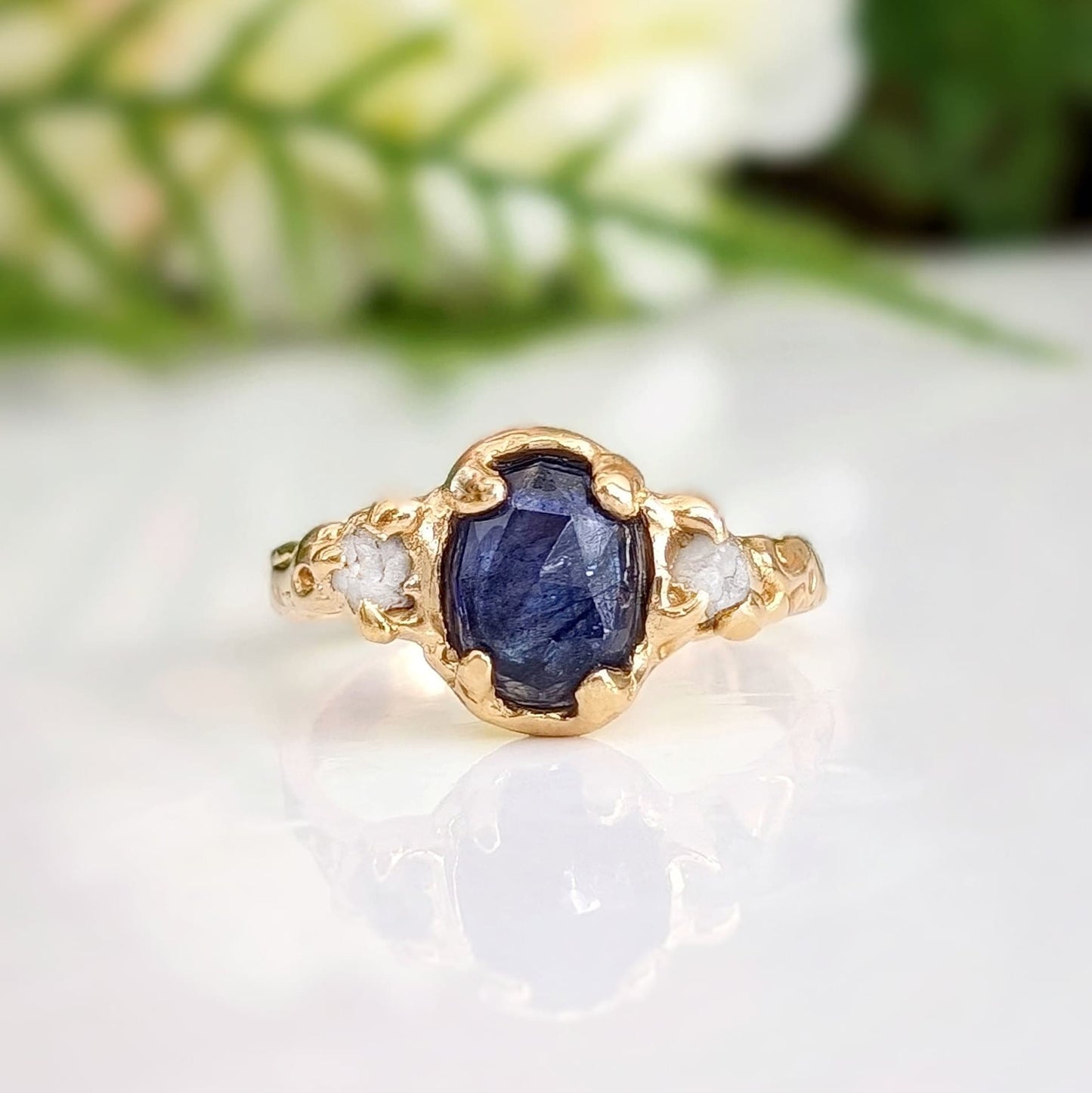 Blue sapphire and diamond engagement ring in solid gold with textured band and nature-inspired design.