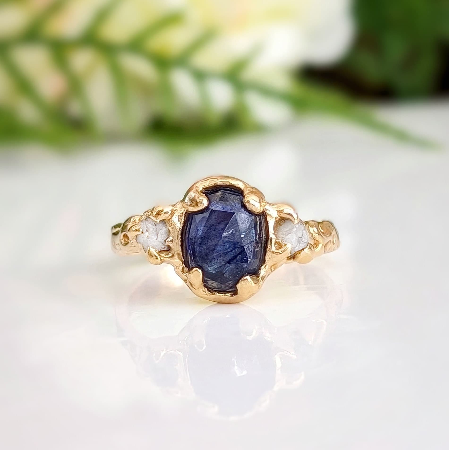 Blue sapphire and diamond engagement ring in solid gold with textured band and nature-inspired design.