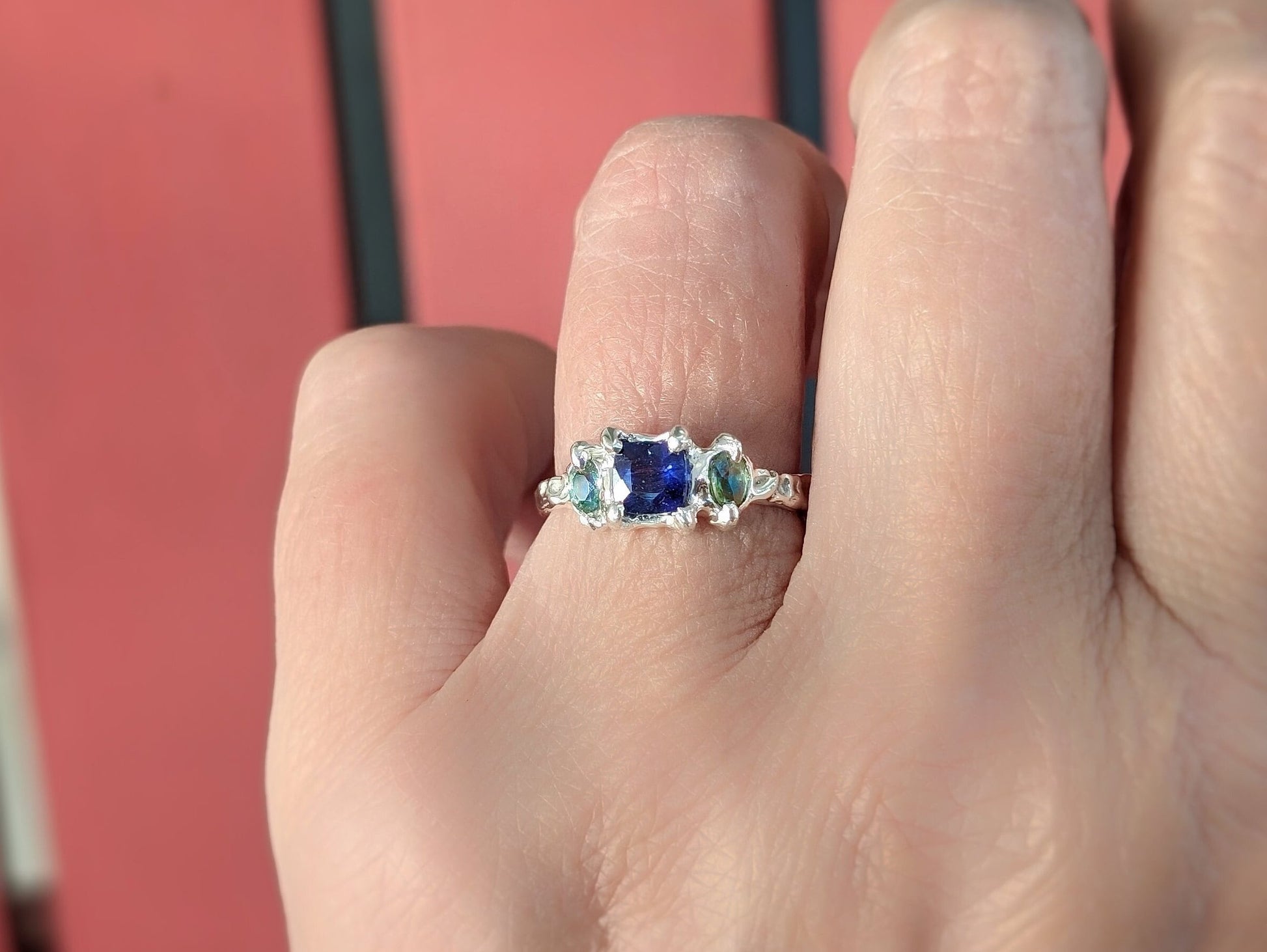 Blue Sapphire and Tourmaline engagement ring in Solid Sterling Silver worn on a hand outdoors.