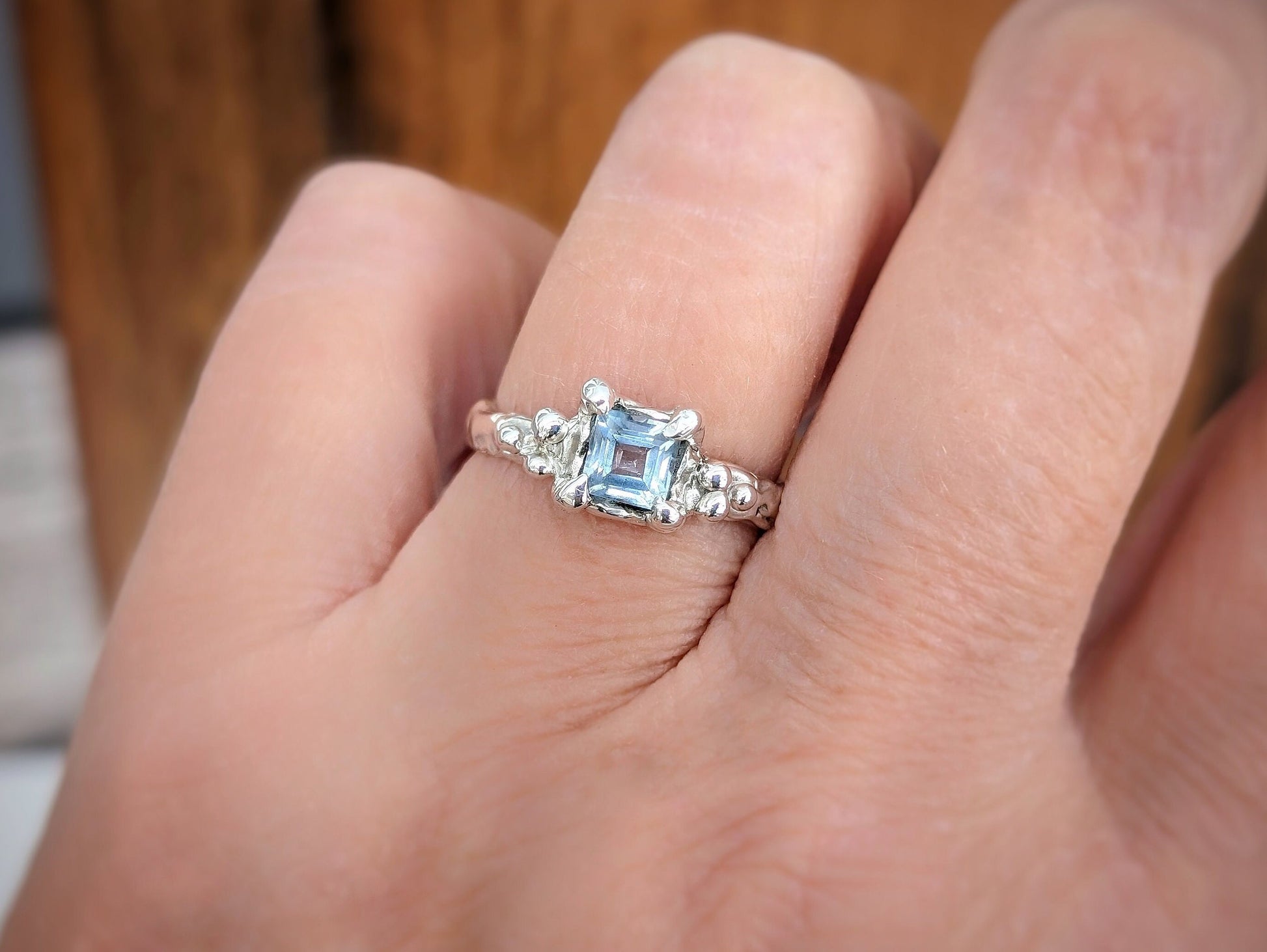 Hand wearing a unique London Blue Topaz engagement ring in solid sterling silver with an organic textured band.