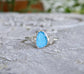 Blue Topaz and Herkimer diamond engagement ring on sterling silver band, showcased on a textured stone surface.
