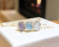 Customized family birthstone ring with purple, blue, and aqua gemstones on a white box background.