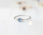 Dainty blue Topaz stacking ring on a reflective surface, featuring a 4mm natural light blue stone in a Sterling Silver band.