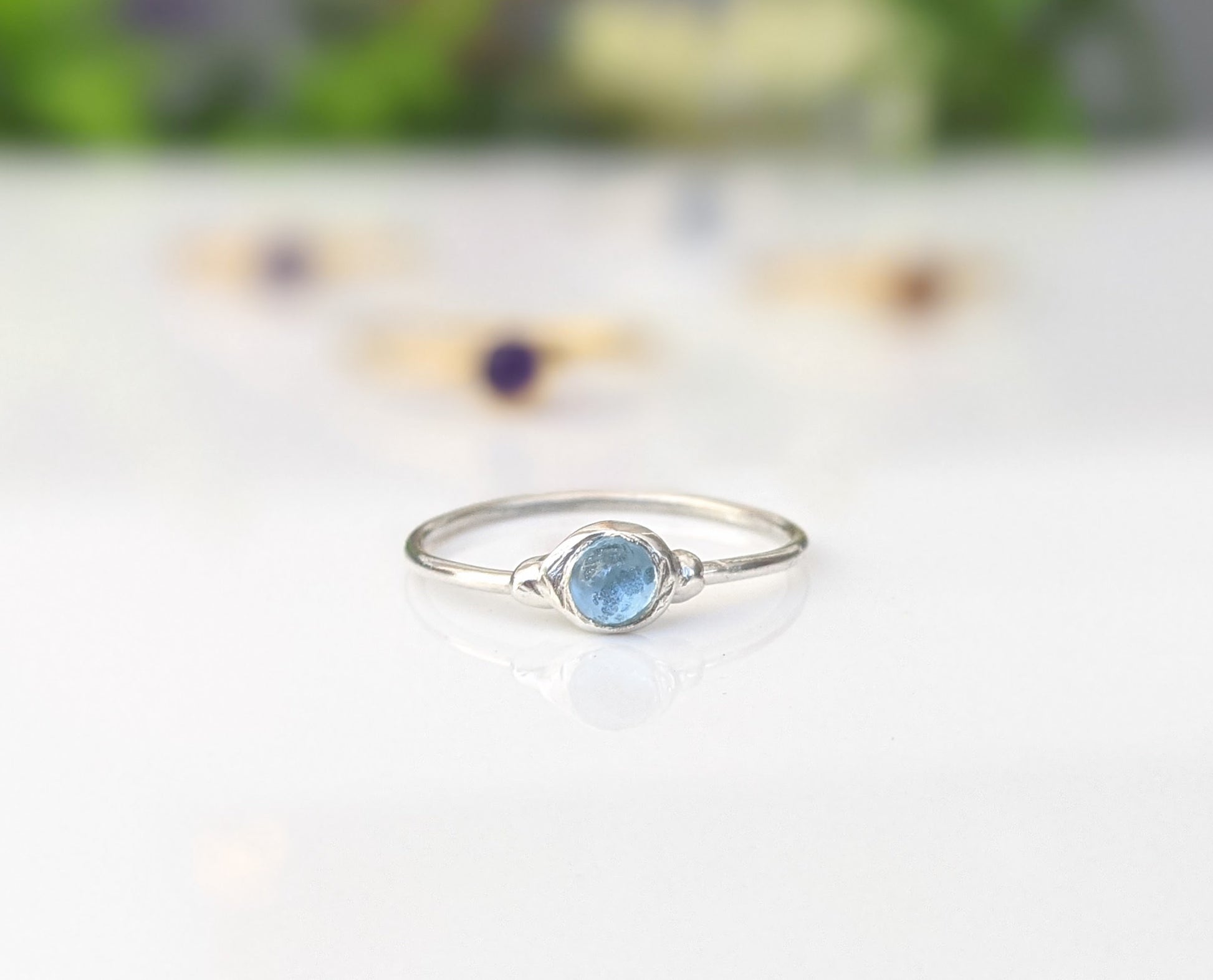 Dainty blue topaz stacking ring on a silver band, perfect for everyday wear and stacking with other rings.