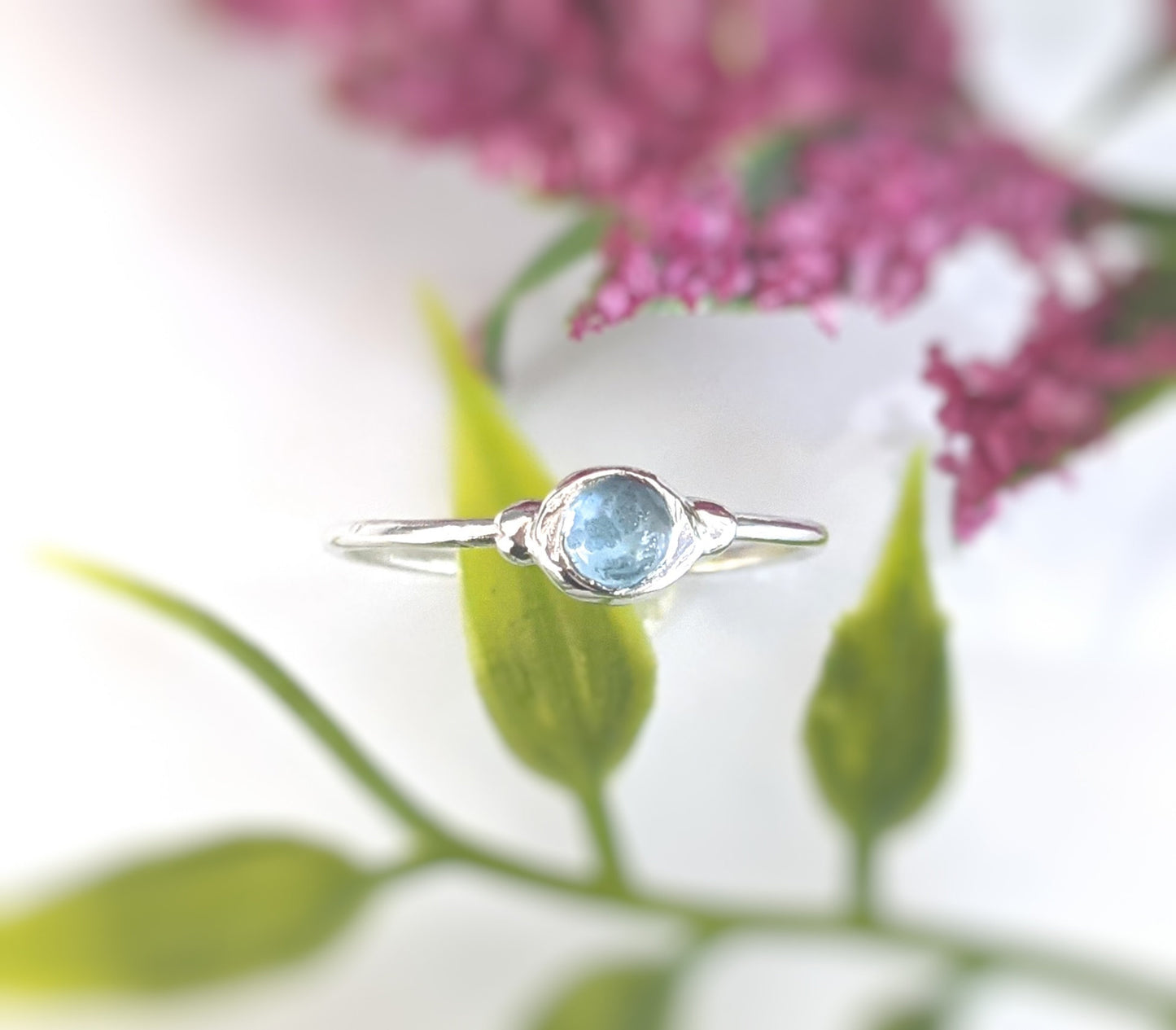 Dainty blue Topaz stacking ring on a silver band against a floral background, perfect for everyday wear.