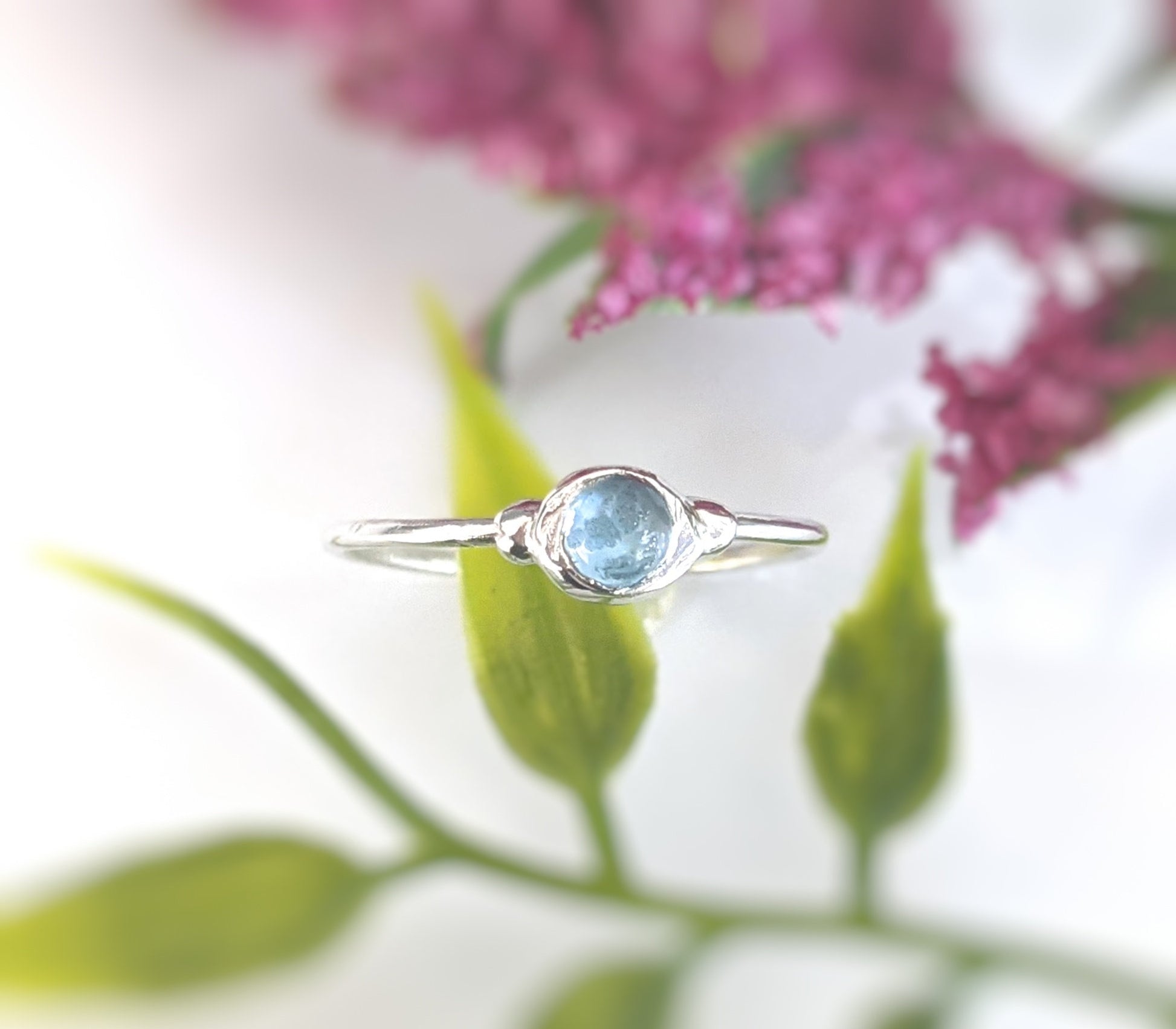 Dainty blue Topaz stacking ring on a silver band against a floral background, perfect for everyday wear.