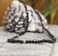 Elegant black spinel bead necklace on a textured stone background, showcasing handcrafted beauty and shine.