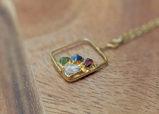 Gold-filled family birthstone necklace with colorful raw gemstones on a wooden surface.