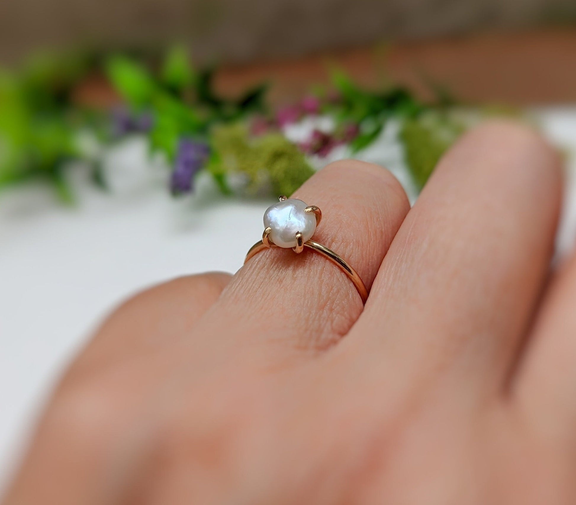 Handcrafted freshwater Keshi pearl ring in 18k gold on a hand, surrounded by greenery, showcasing elegance.