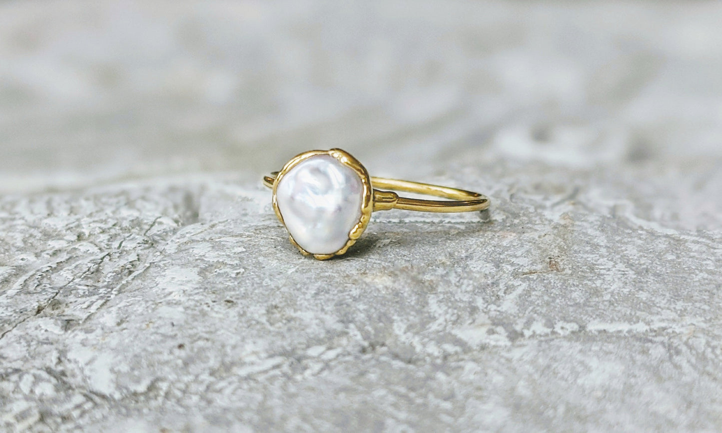 Small freshwater Keshi pearl ring on a textured surface, featuring a solid 14k gold band and a luminous pearl.
