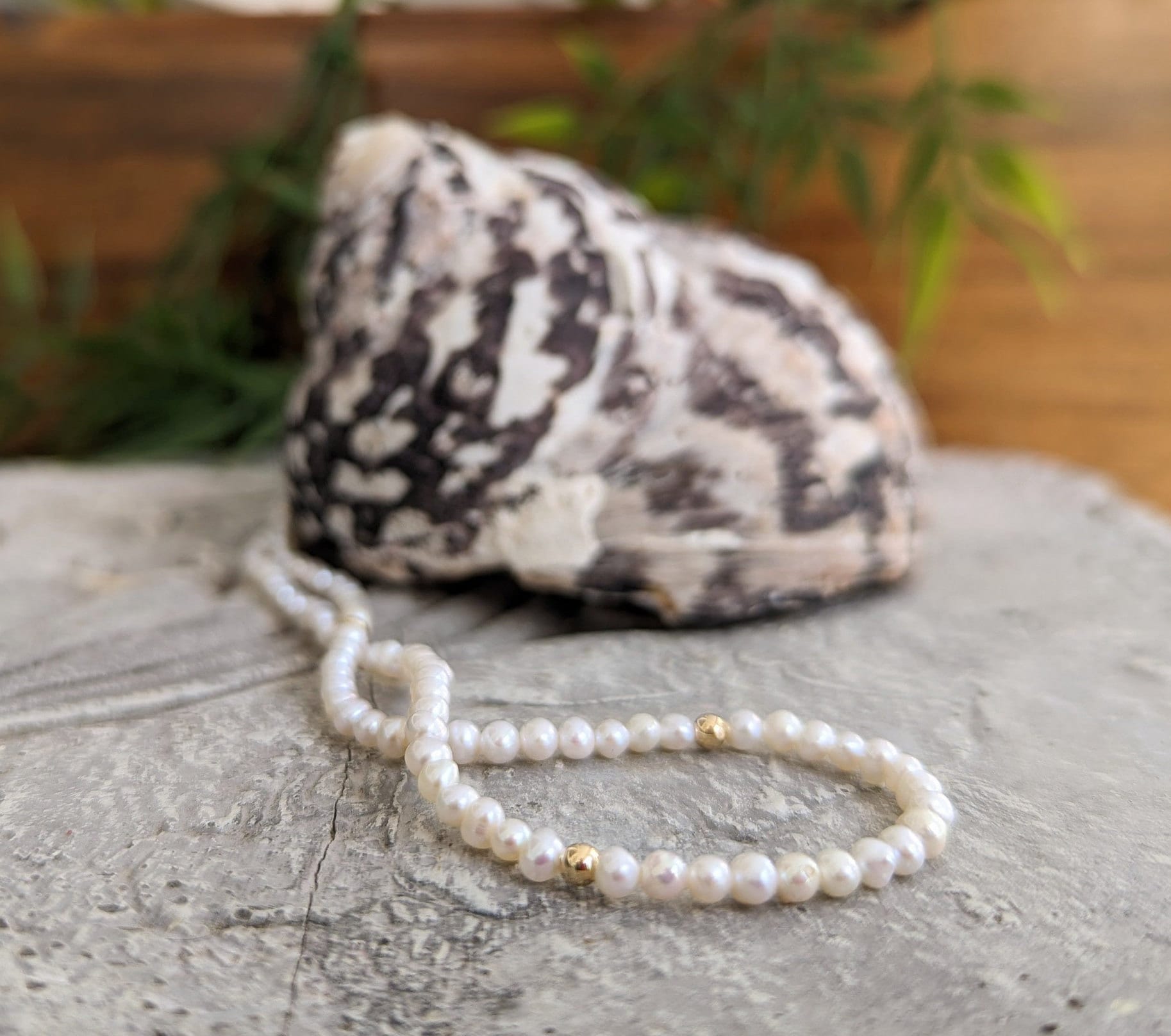 Handmade freshwater pearl necklace with gold accents displayed on a natural stone surface.