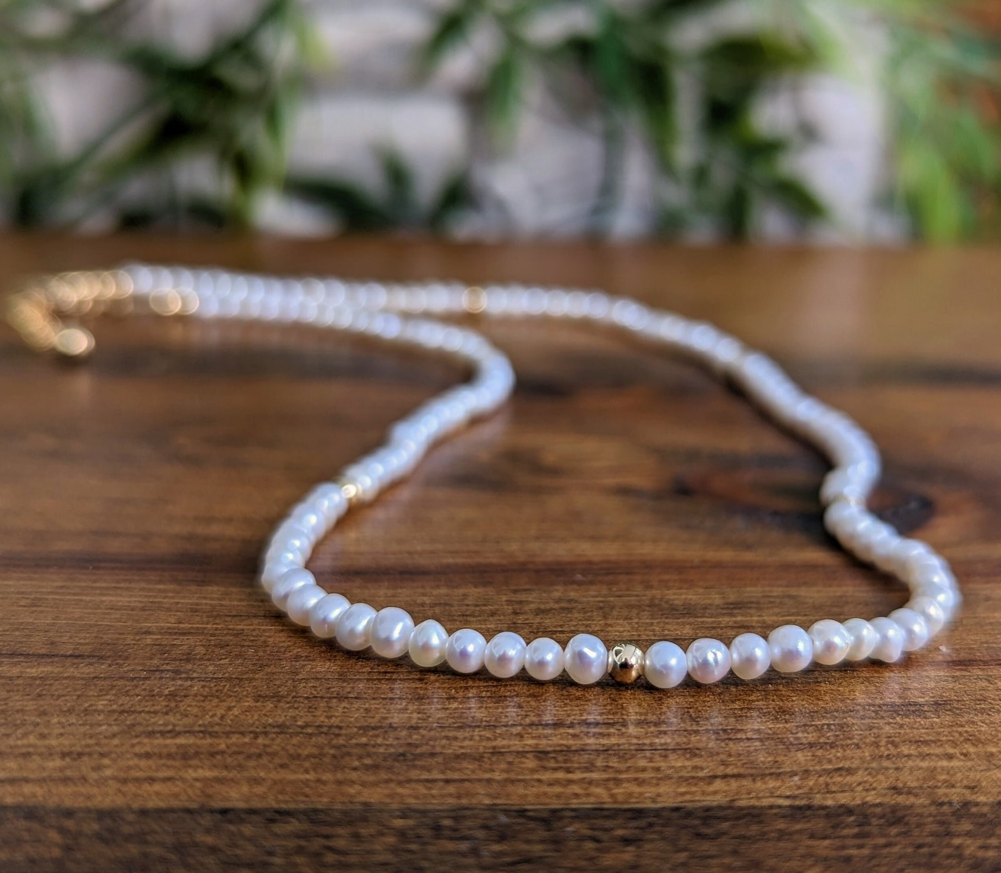 Delicate freshwater pearl necklace with gold accents on wooden background, perfect for weddings and as a Mother's Day gift.