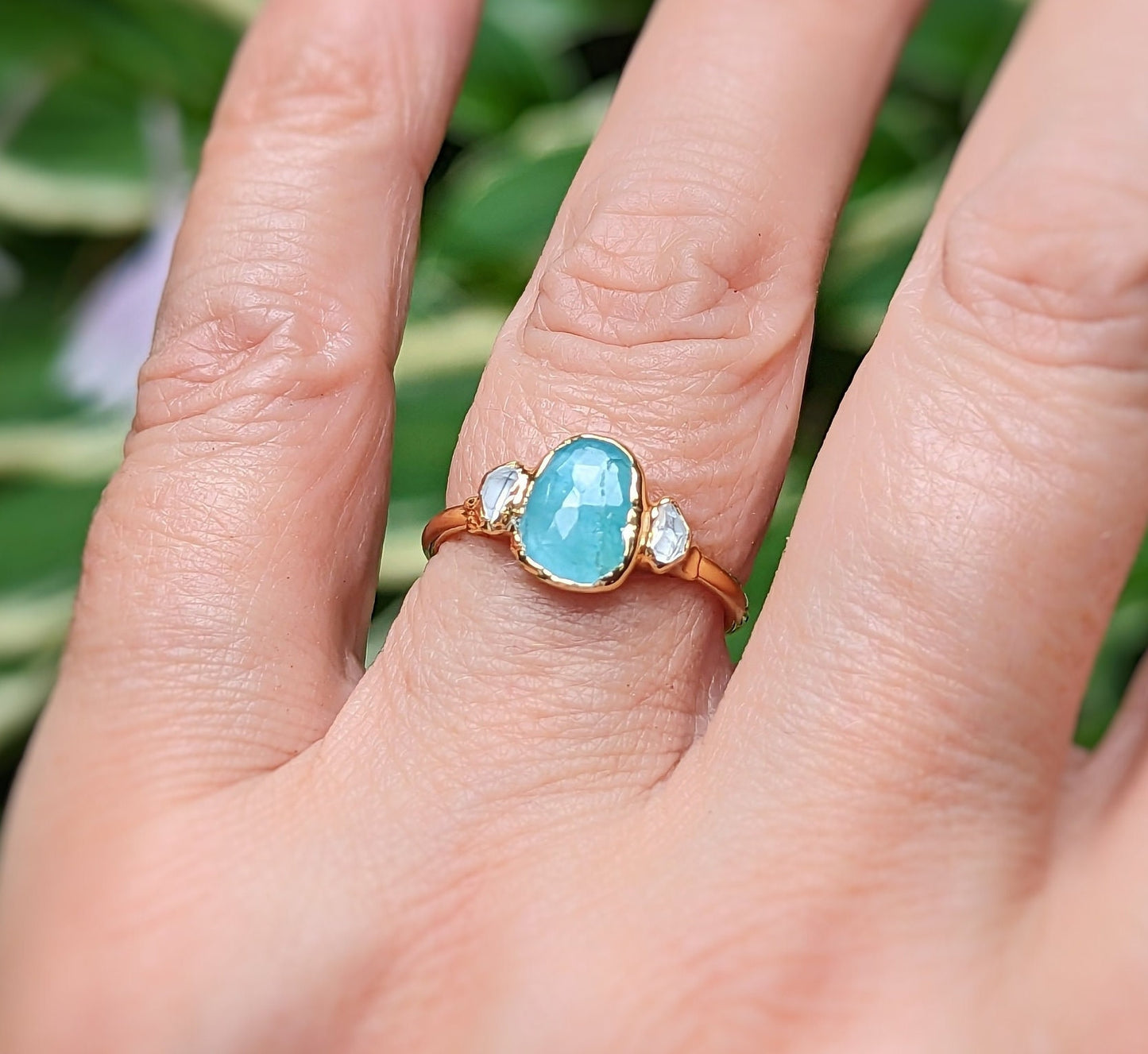 Aqua blue Grandidierite and diamond ring in 18k gold, elegantly worn on a hand surrounded by greenery.