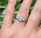 Aqua blue Grandidierite and diamond ring in 18k gold, elegantly worn on a hand surrounded by greenery.