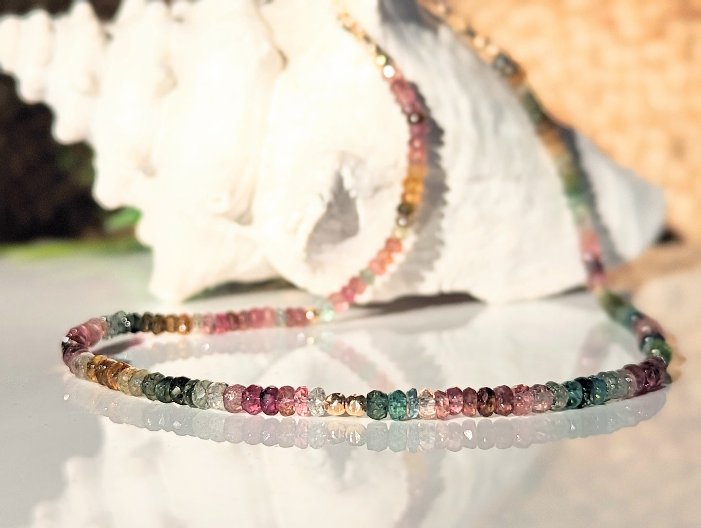 Handcrafted Multi Tourmaline bead necklace showcasing vibrant colors on a reflective surface.