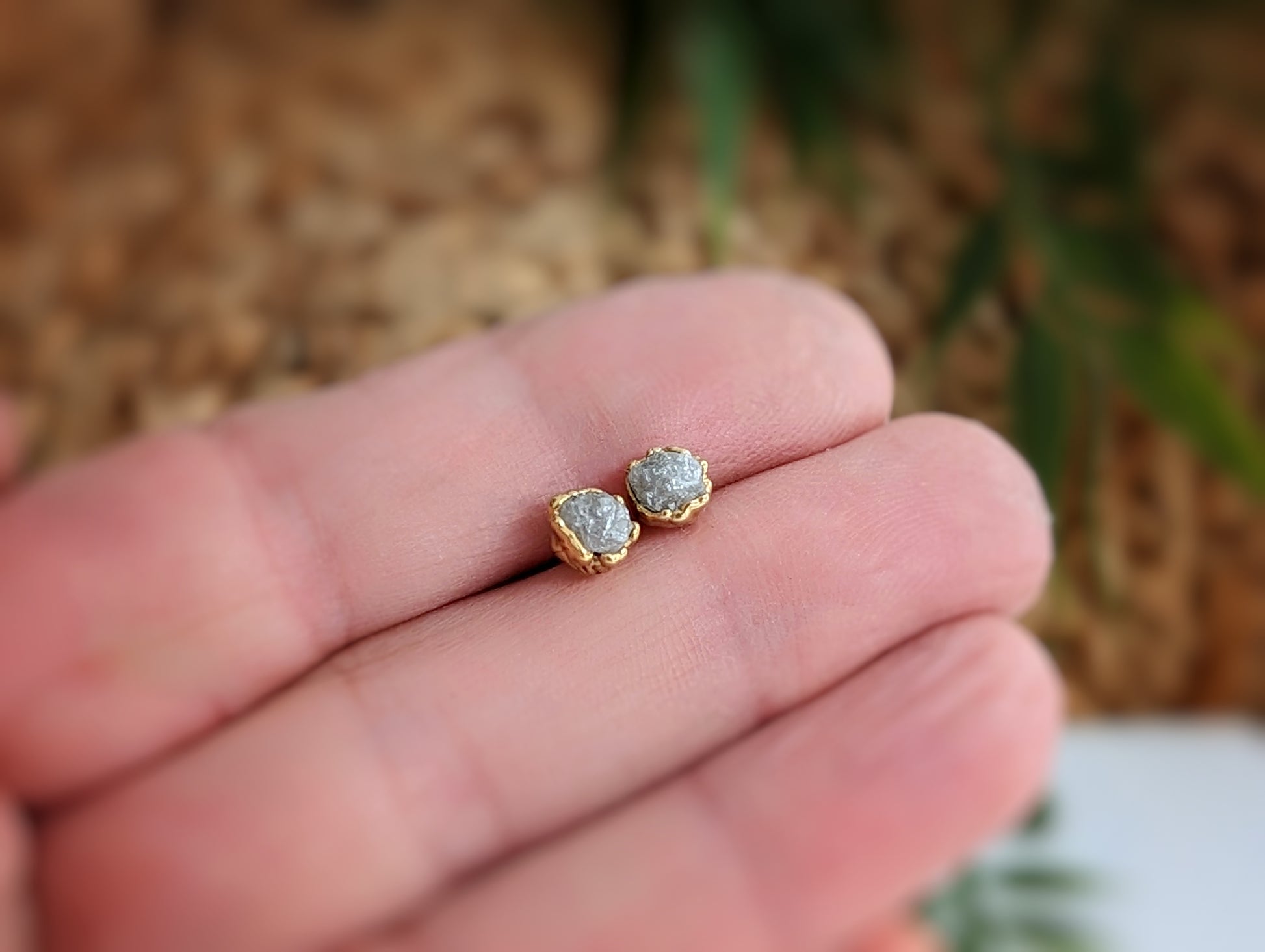 Raw diamond stud earrings in gold settings held in a hand, showcasing their natural, uncut beauty.