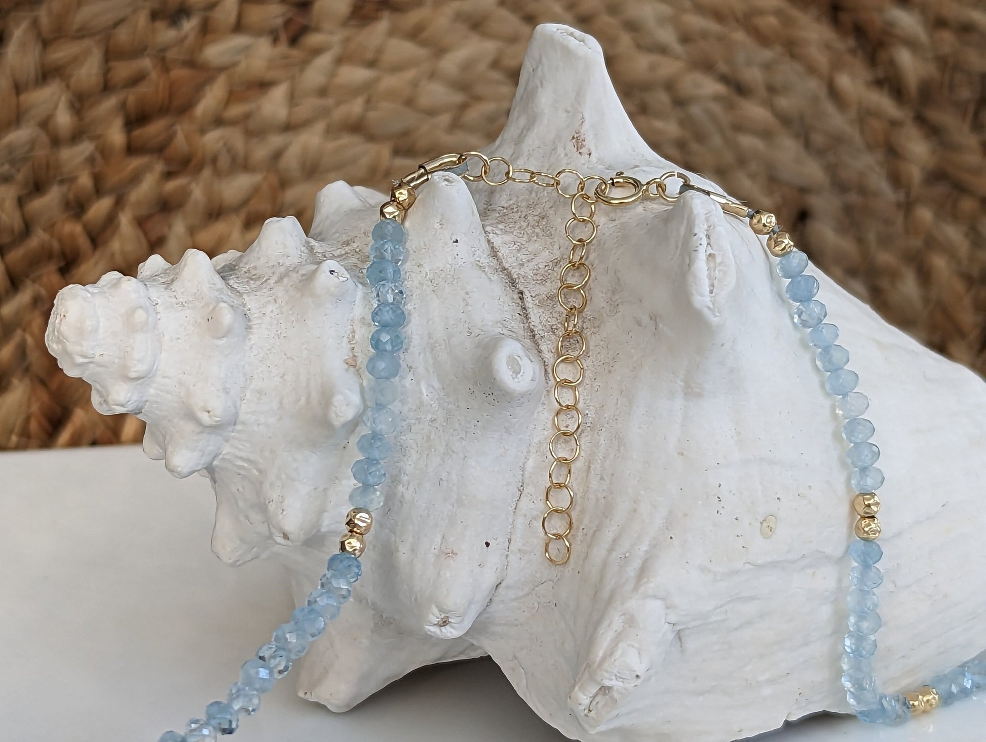 Handmade aquamarine bead necklace with gold accents resting on a seashell, symbolizing calmness and serenity.