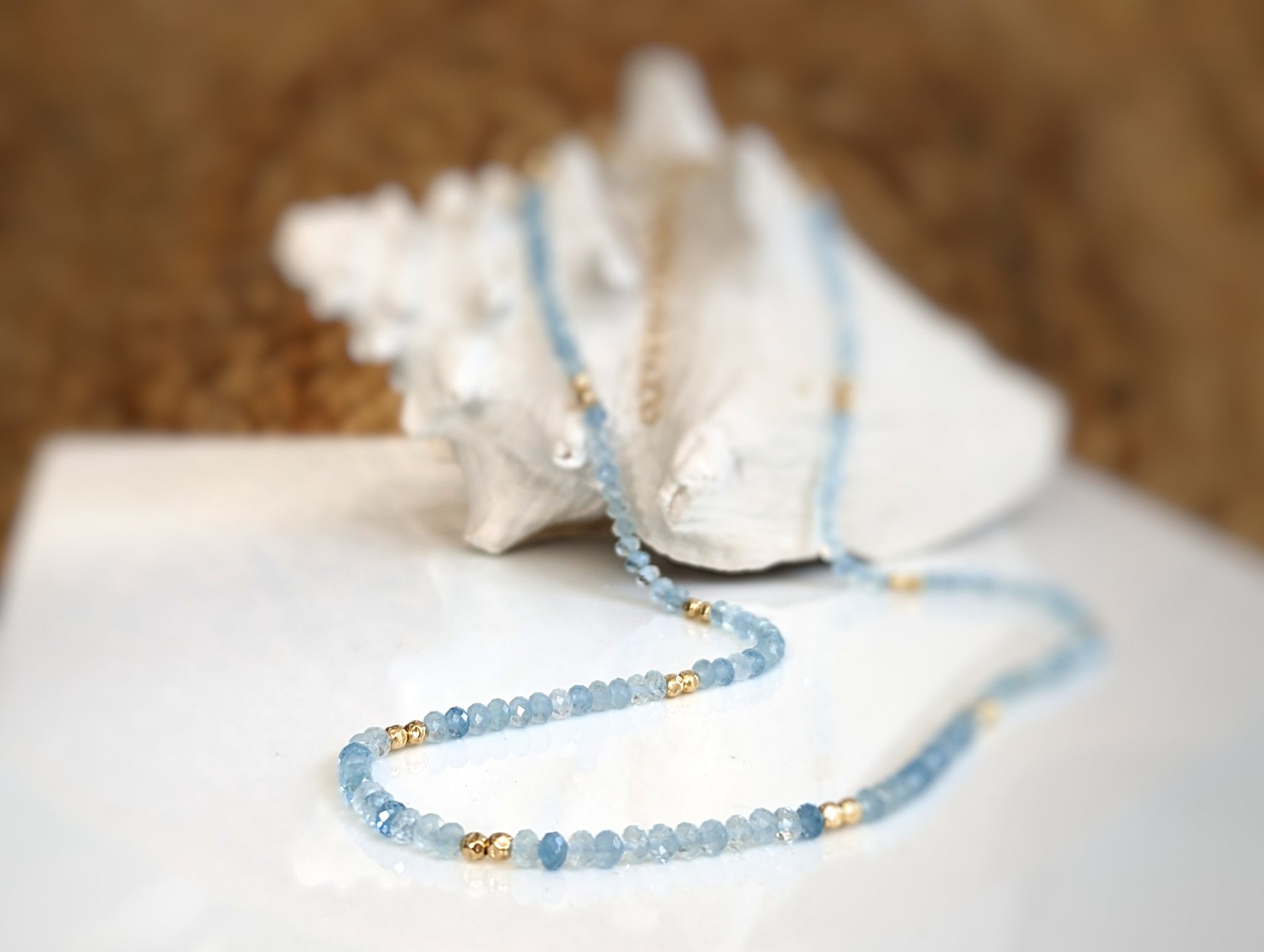Handmade aquamarine bead necklace with gold accents on a shell background, symbolizing calmness and serenity.