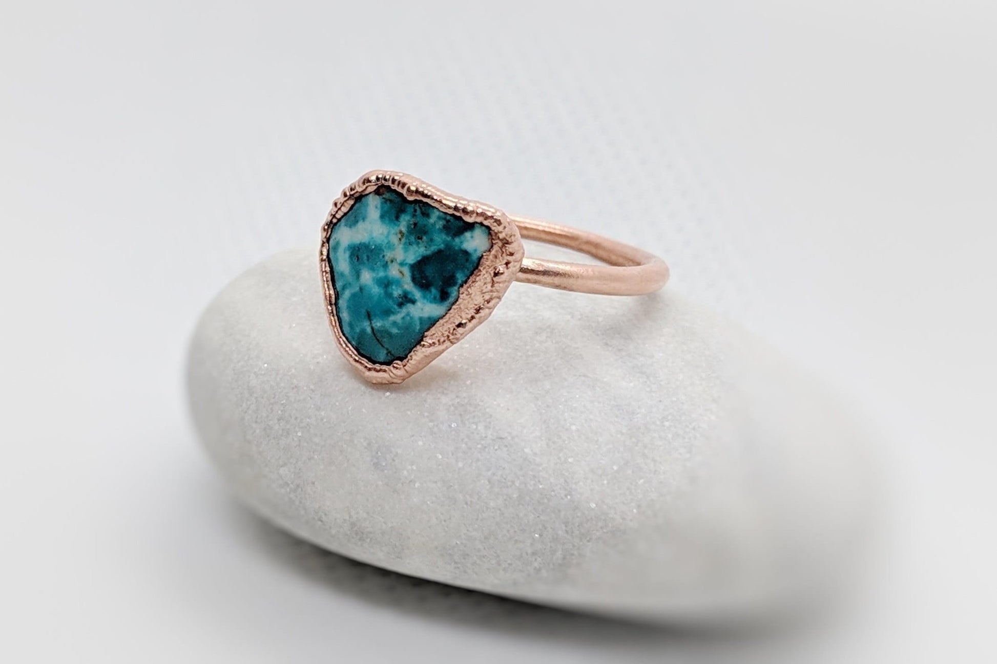 Natural turquoise ring with a unique heart shape, set in rose gold on a smooth stone background.