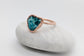 Natural turquoise ring with a unique heart shape, set in rose gold on a smooth stone background.