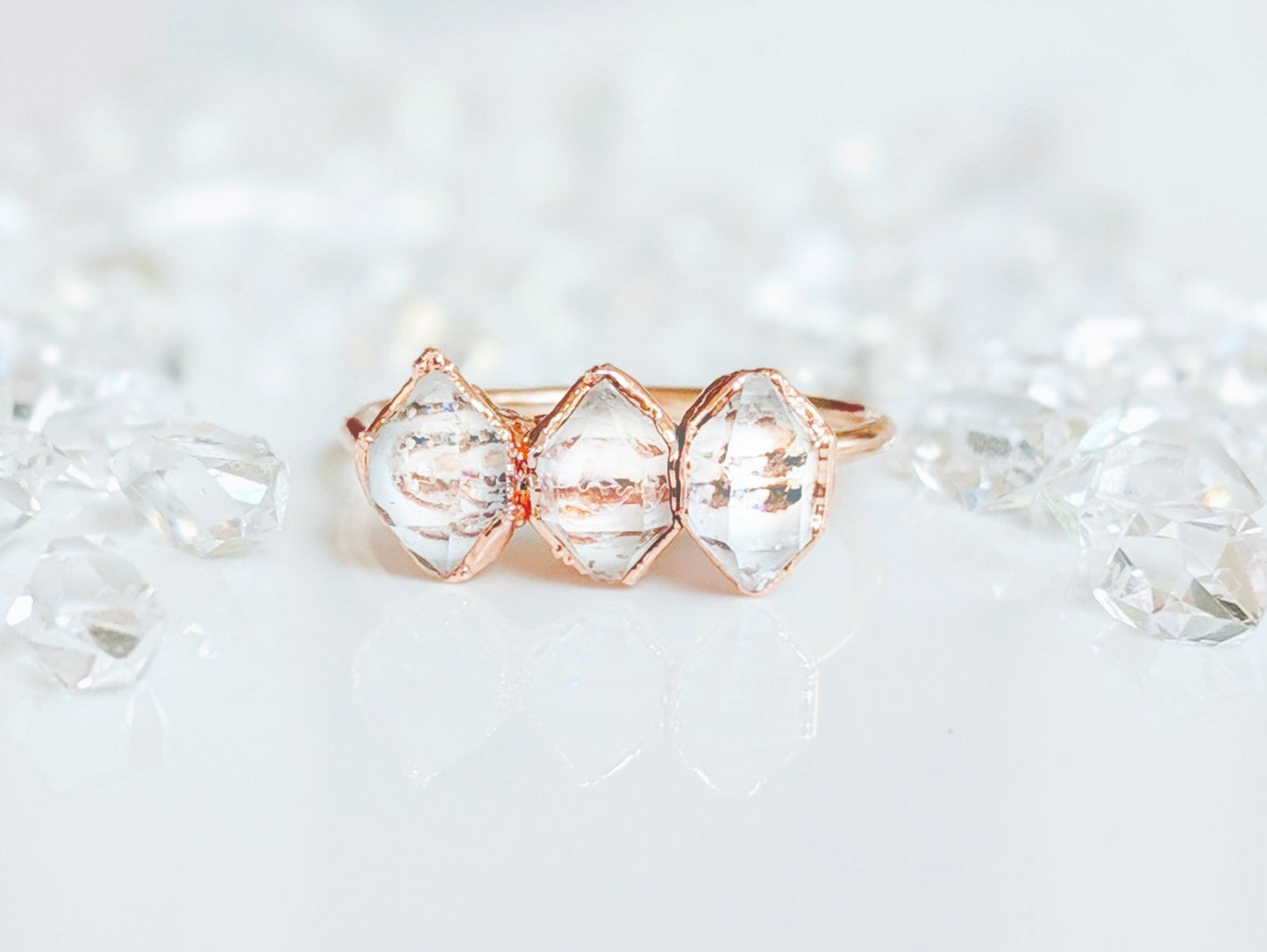 Handcrafted triple Herkimer diamond ring on a reflective surface with scattered crystals, perfect for everlasting love.