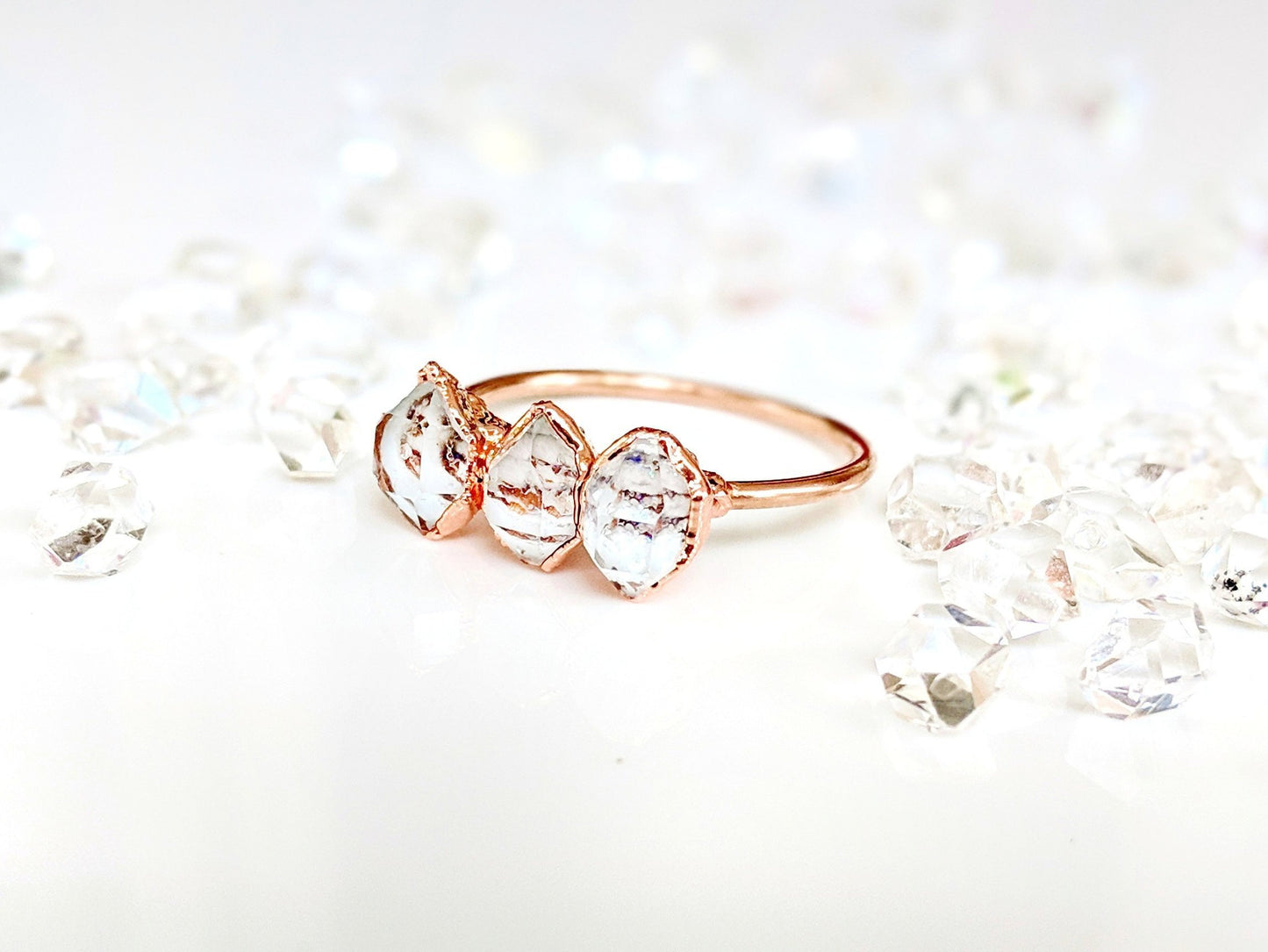 Triple Herkimer diamond ring on a delicate gold band, surrounded by sparkling quartz crystals.