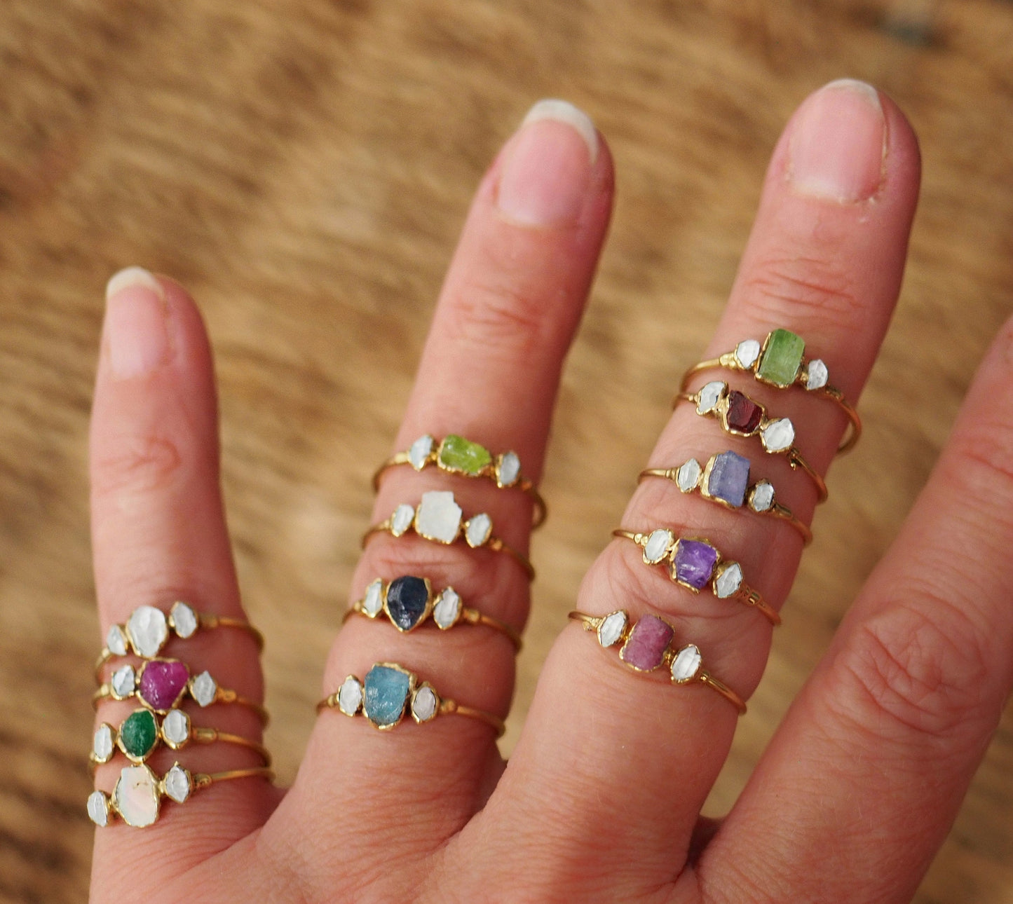 Multiple gold-filled rings featuring raw gemstones and Herkimer diamonds displayed on a hand.