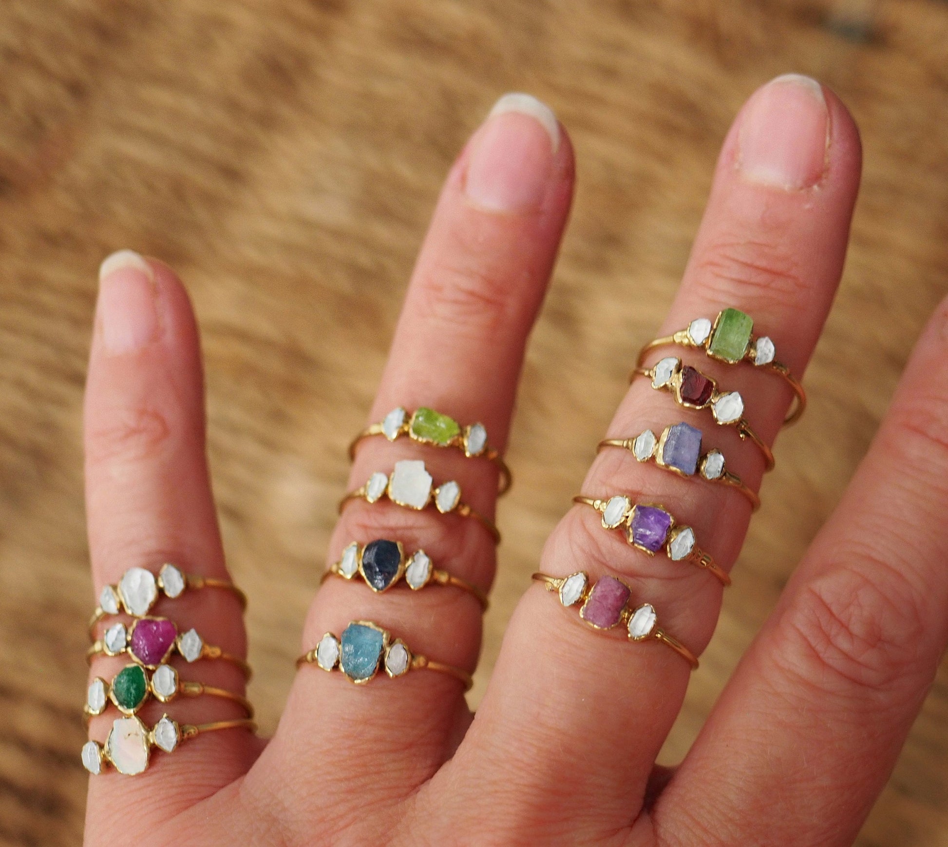Multiple gold-filled rings featuring raw gemstones and Herkimer diamonds displayed on a hand.