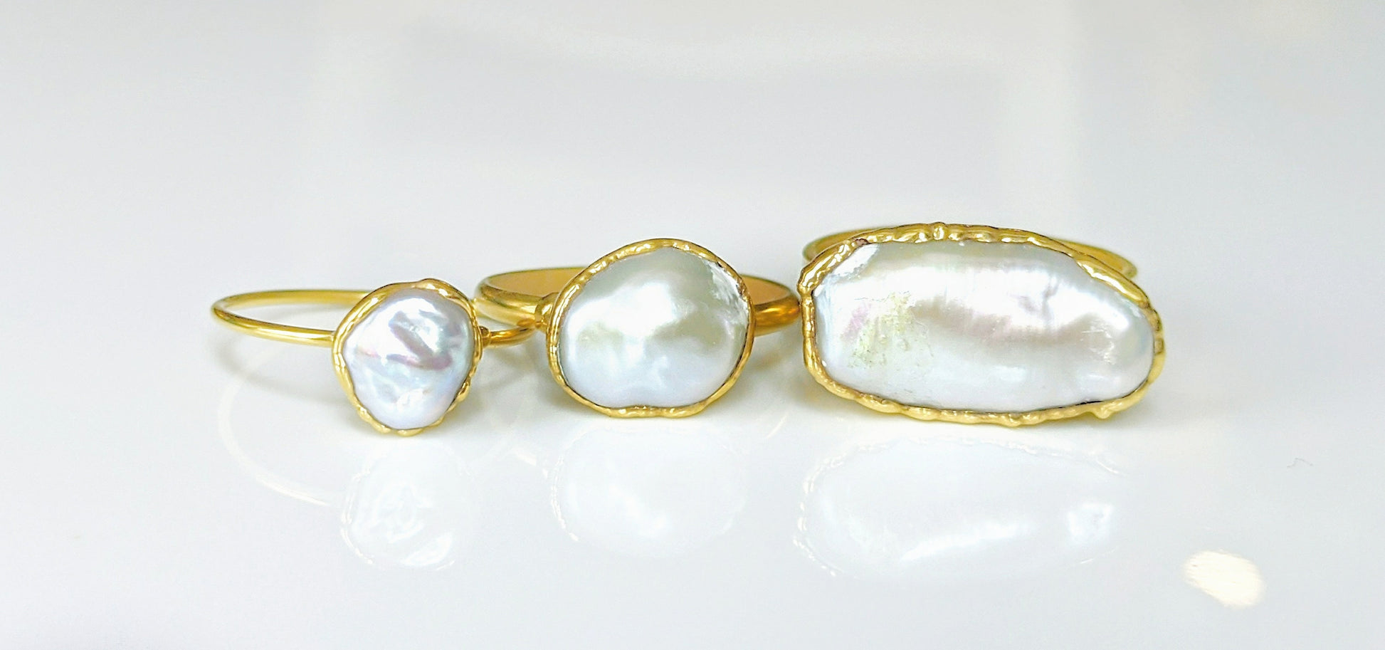 Three handmade Keshi pearl rings on gold bands showcasing unique shapes and luster.