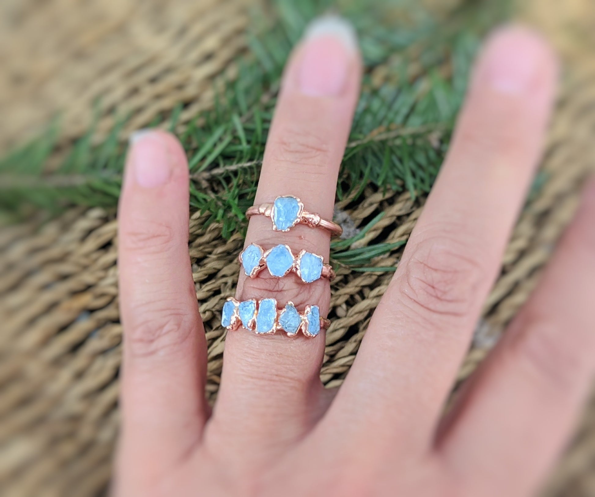 Three raw Aquamarine rings with a rose gold setting showcased on a hand, perfect for showcasing March's birthstone.