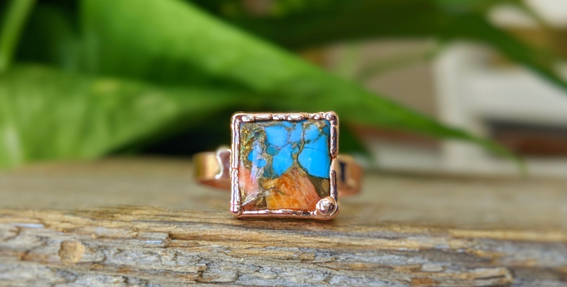 Handcrafted Pink Opal Copper Turquoise ring on a wooden surface with greenery in the background.