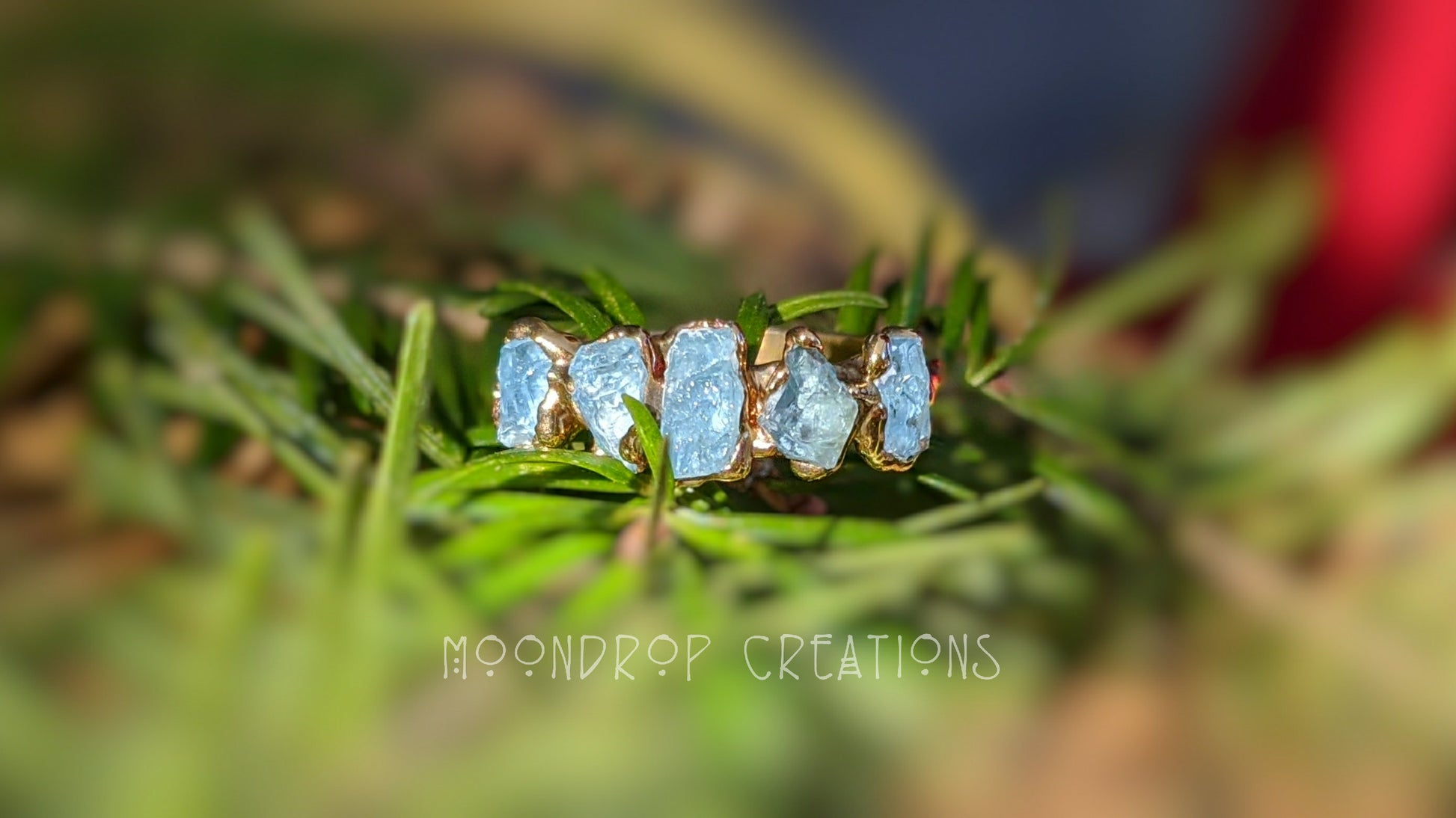 Raw Aquamarine Eternity ring featuring five natural stones on a 14k Gold filled band, against a green background.