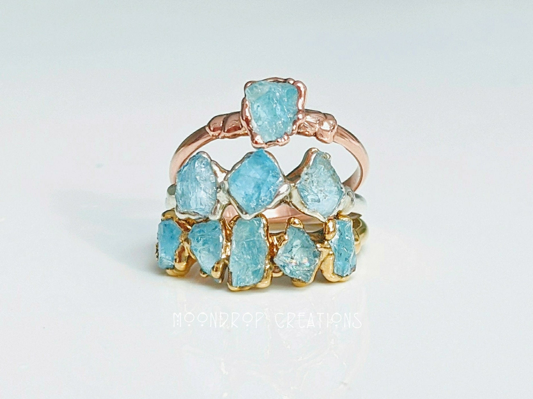Raw aquamarine rings stacked, featuring natural stones set on gold and rose gold bands, perfect for March birthdays.