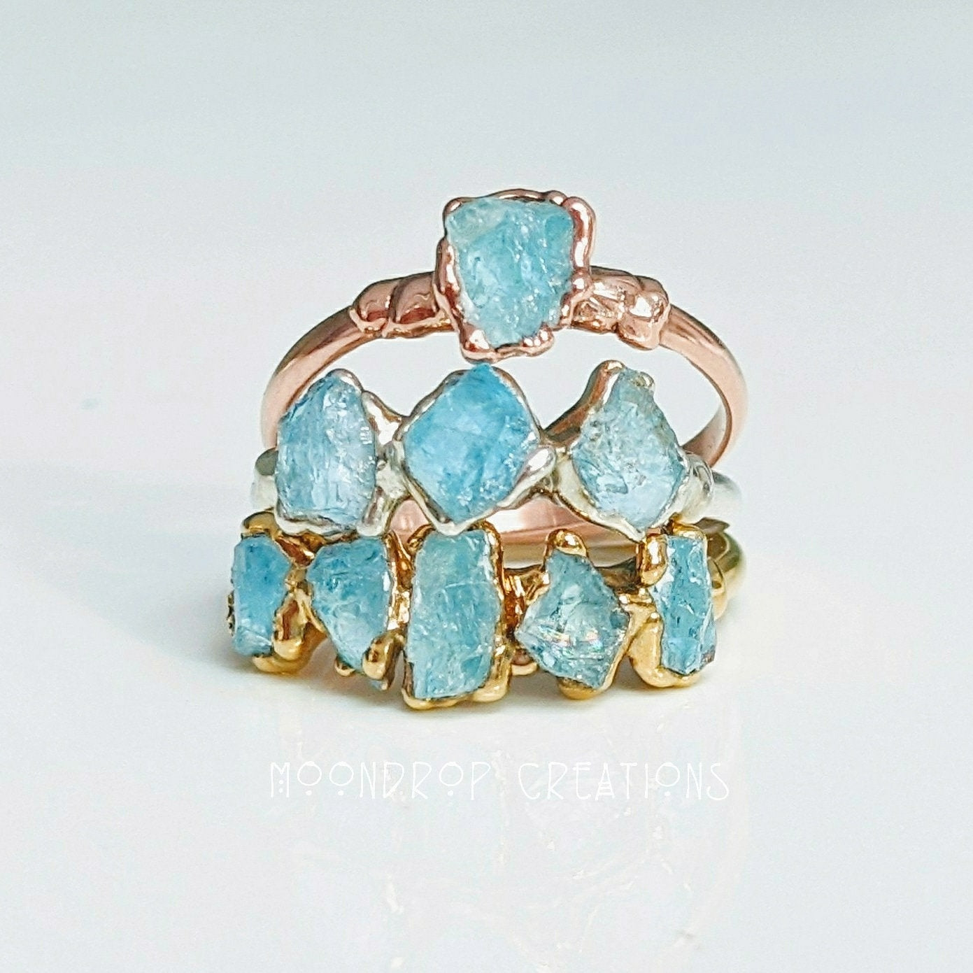 Raw Aquamarine rings in gold and rose gold, showcasing natural gemstones on a minimalist display.