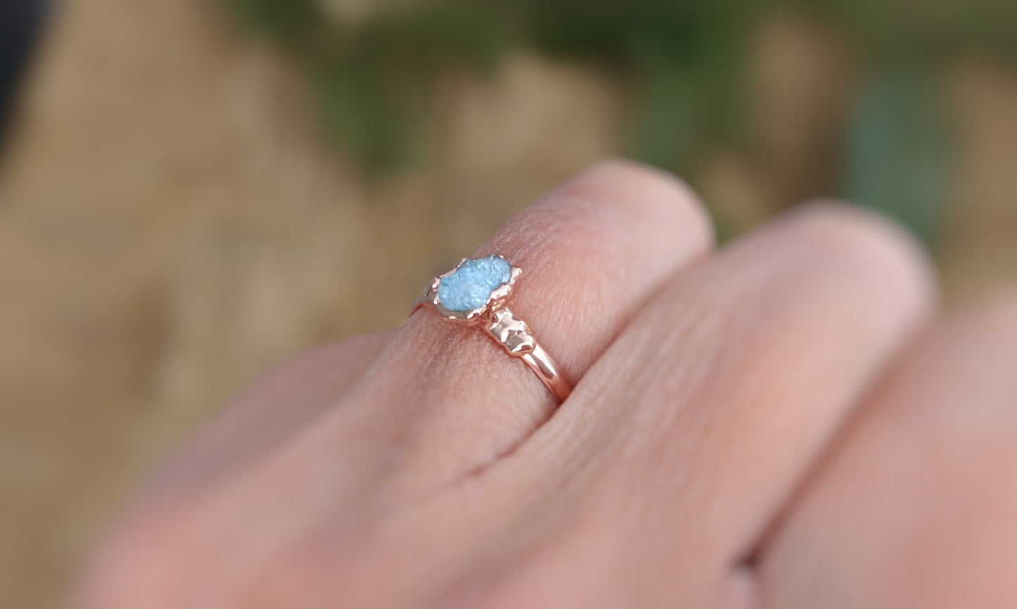 Raw Aquamarine ring on a hand, featuring a 14k Gold filled band and sparkling gemstone.