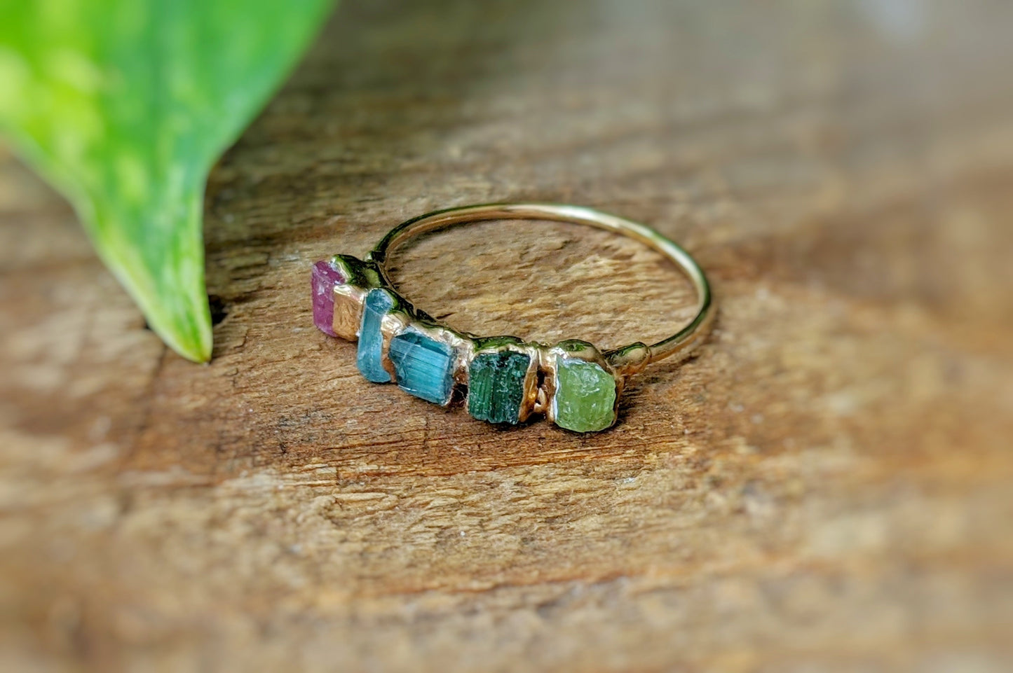 Colorful raw Tourmaline eternity ring on a wooden surface, featuring five multi-color stones set on a gold band.
