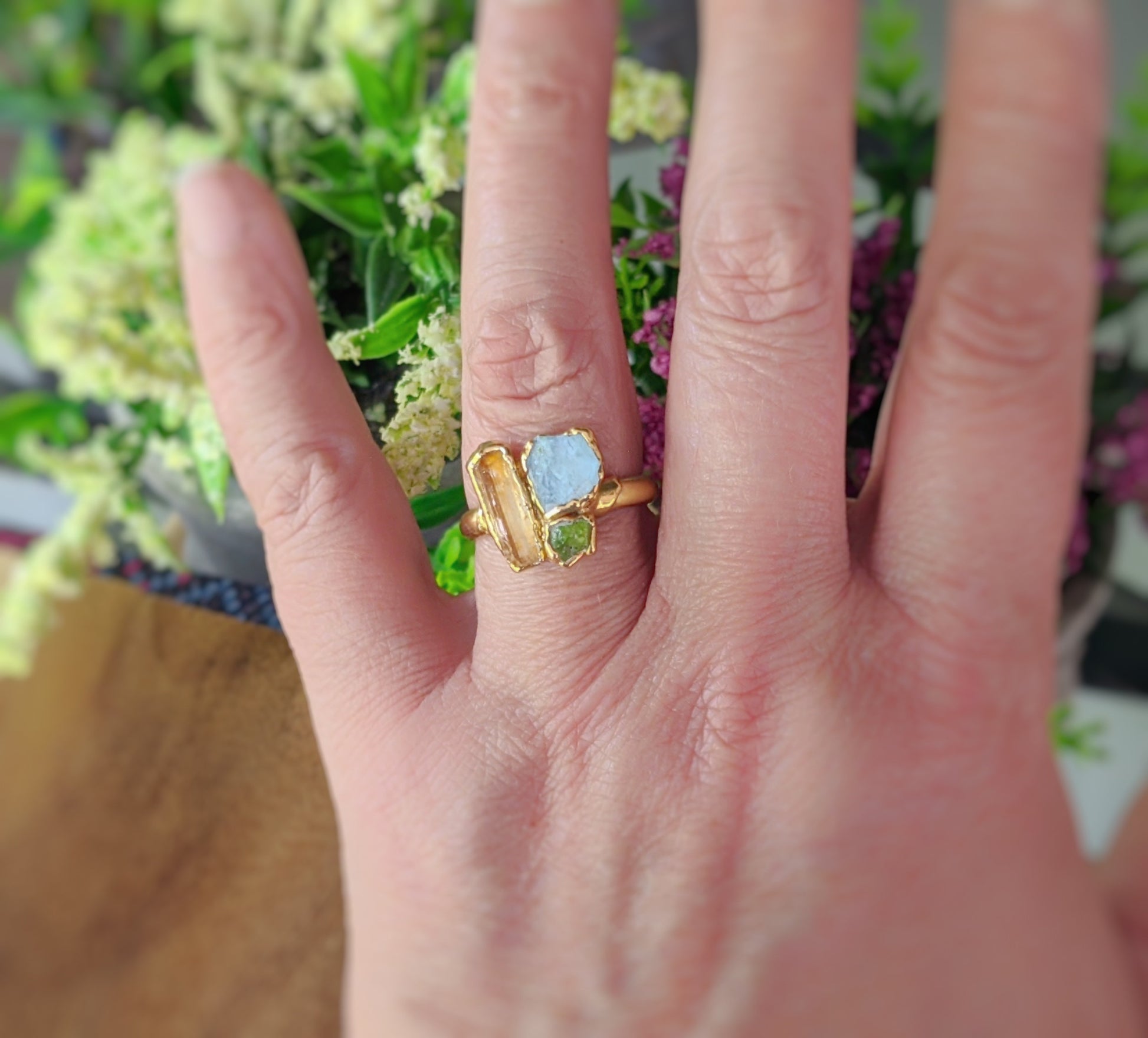 Close-up of a raw gemstone cluster ring featuring golden imperial topaz, aquamarine, and peridot on a hand.